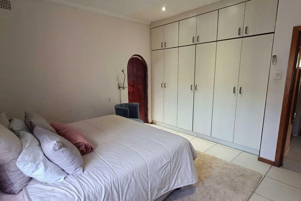 A bedroom featuring extensive floor-to-ceiling built-in cupboards, tiled flooring, and a distinctive arched doorway.