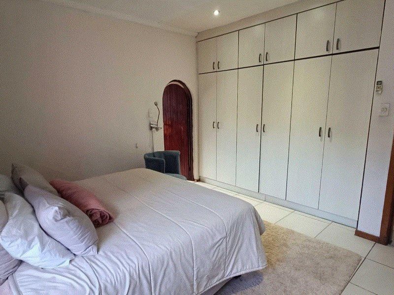 A bedroom featuring extensive floor-to-ceiling built-in cupboards, tiled flooring, and a distinctive arched doorway.