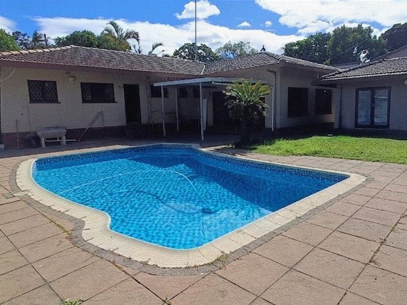 Rear exterior view featuring a swimming pool, paved patio area, and covered outdoor space with a tiled roof.