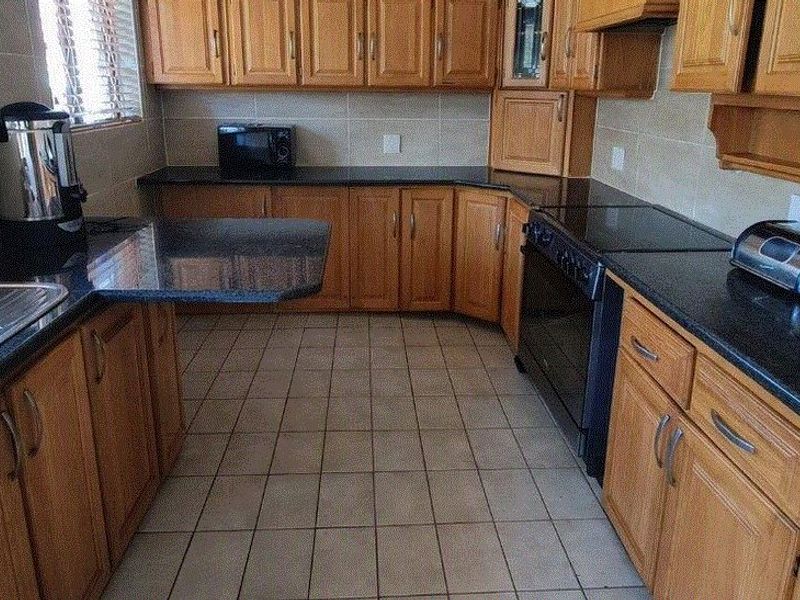 A functional kitchen featuring wooden cabinetry, granite countertops, tiled flooring, and built-in cooking appliances with a tiled backsplash.
