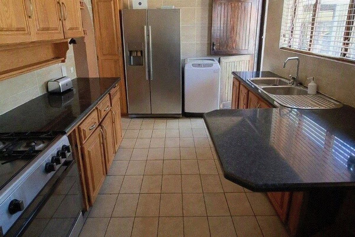 A functional kitchen featuring wooden cabinetry, dark granite countertops, a gas stove, and tiled flooring with direct access to the exterior.