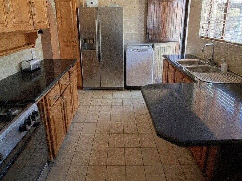 A functional kitchen featuring wooden cabinetry, dark granite countertops, a gas stove, and tiled flooring with direct access to the exterior.