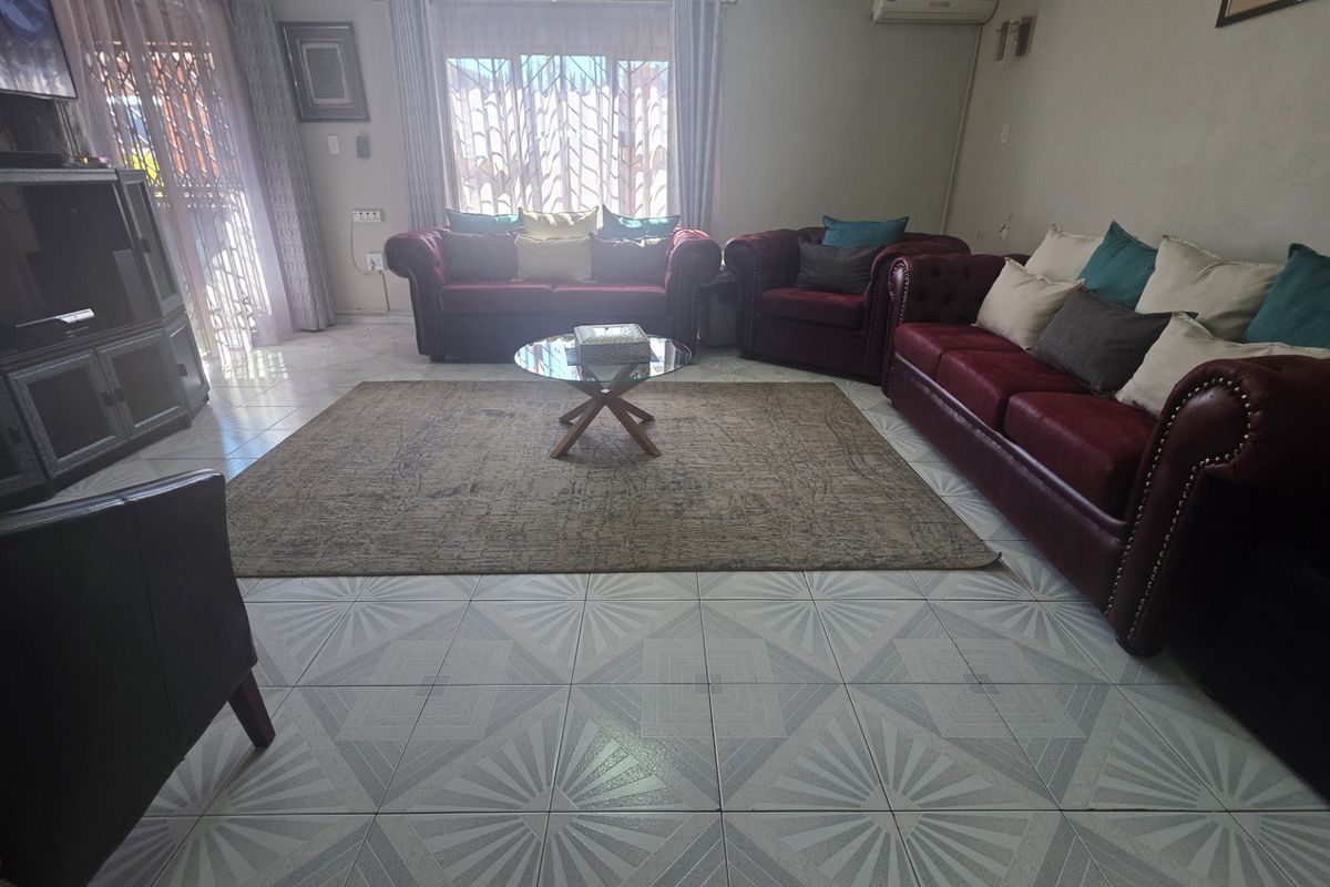 A spacious living room featuring tiled flooring, an installed air conditioning unit, and natural light through large windows with security gates.