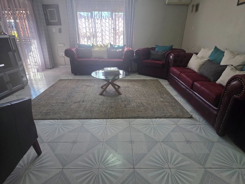 A spacious living room featuring tiled flooring, an installed air conditioning unit, and natural light through large windows with security gates.