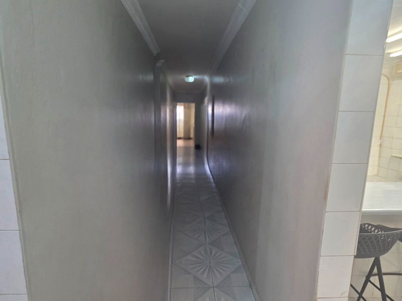 A narrow, tiled hallway connecting living spaces, featuring neutral walls and simple ceiling lighting.