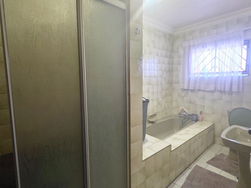 A dated bathroom featuring a built-in bathtub, separate shower enclosure, and pedestal sink with original ceramic wall tiling.
