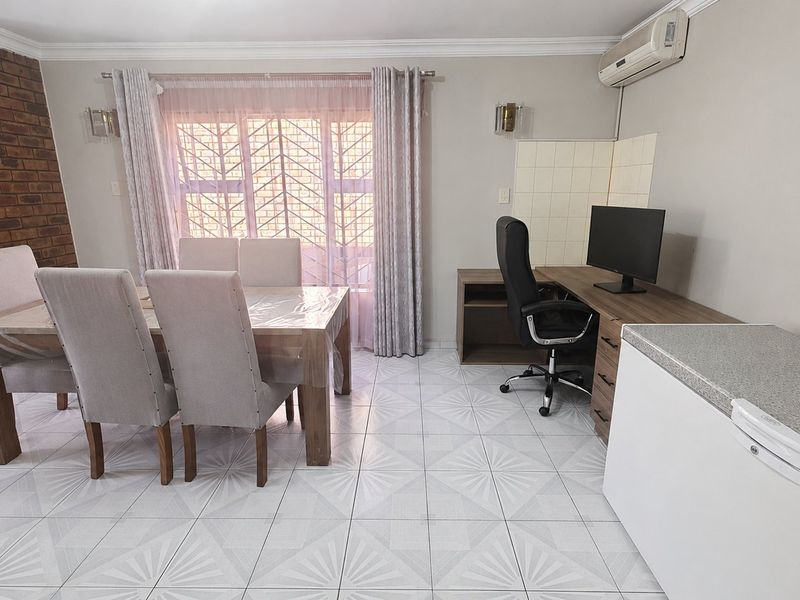 Open plan living area featuring tiled flooring, a brick feature wall, built-in desk space, and a wall-mounted air conditioning unit.