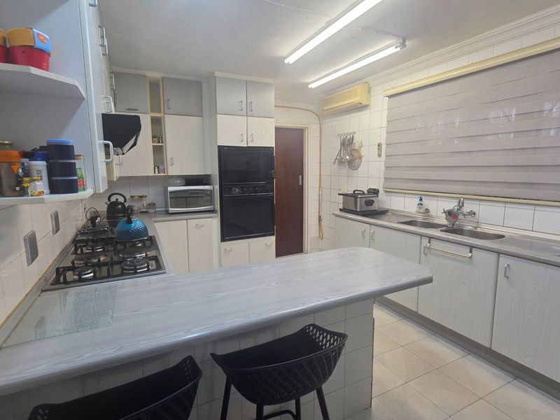Functional kitchen featuring a gas hob, built-in oven, double sink, and ample cabinetry with a breakfast bar counter.