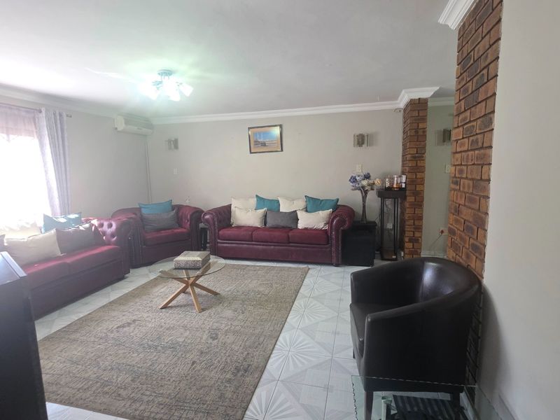 Spacious living room featuring ceramic floor tiles, an exposed brick pillar, and a wall-mounted air conditioning unit.