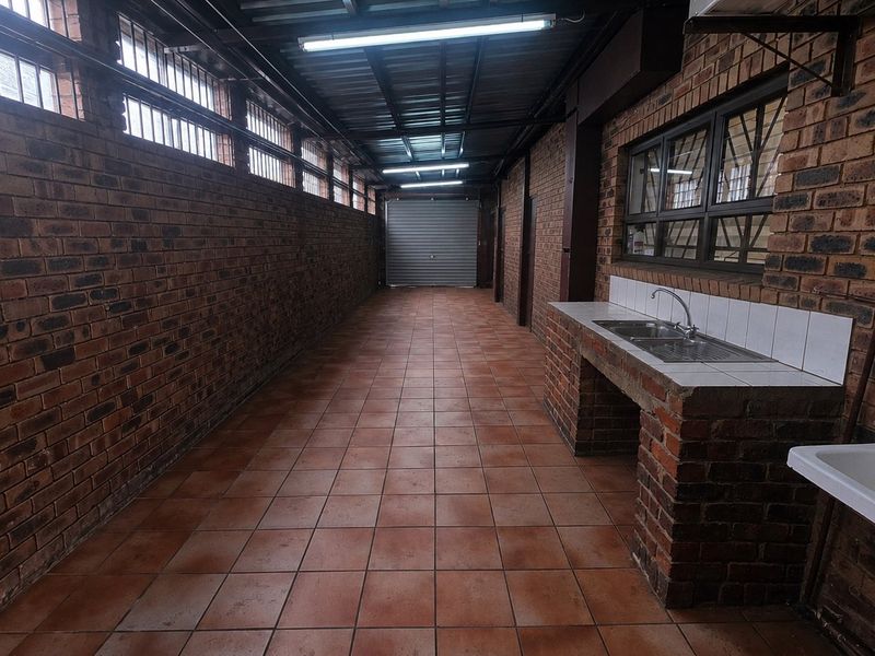 A spacious, functional laundry area featuring exposed brick walls, tiled flooring, a built-in brick sink counter, and a secure roller shutter door.