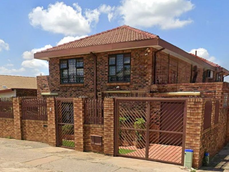 A two-story face brick house featuring a tiled roof, secure perimeter wall with metal gates, and security bars on the windows.