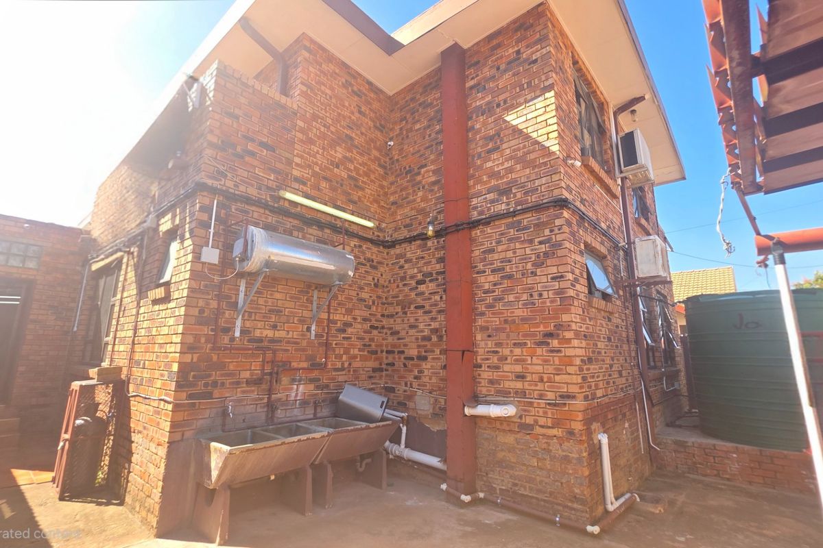 Rear exterior view of a face brick house featuring an external geyser, concrete laundry wash troughs, and a water storage tank.