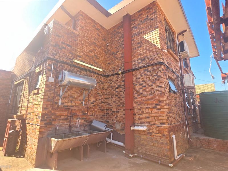 Rear exterior view of a face brick house featuring an external geyser, concrete laundry wash troughs, and a water storage tank.