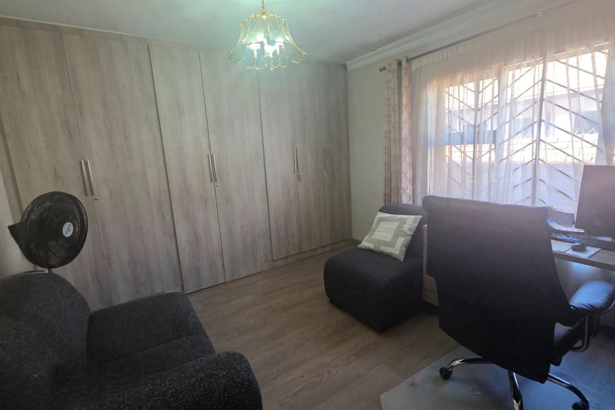 A bedroom featuring extensive built-in cupboards, laminate flooring, and a window fitted with a security gate.