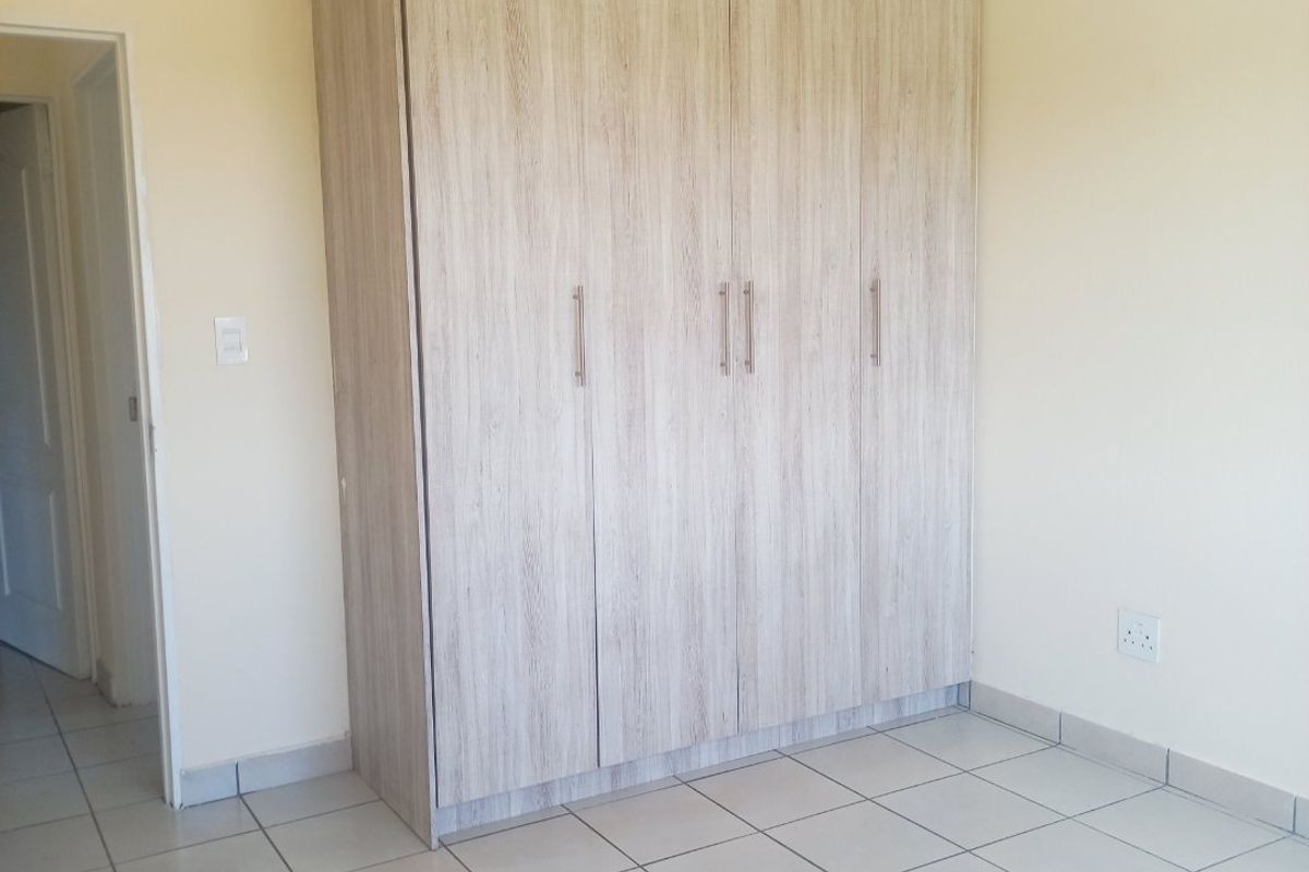 A clean, empty bedroom featuring light-toned built-in cupboards and neutral tiled flooring, providing a versatile space ready for personalization.