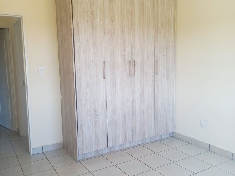 A clean, empty bedroom featuring light-toned built-in cupboards and neutral tiled flooring, providing a versatile space ready for personalization.