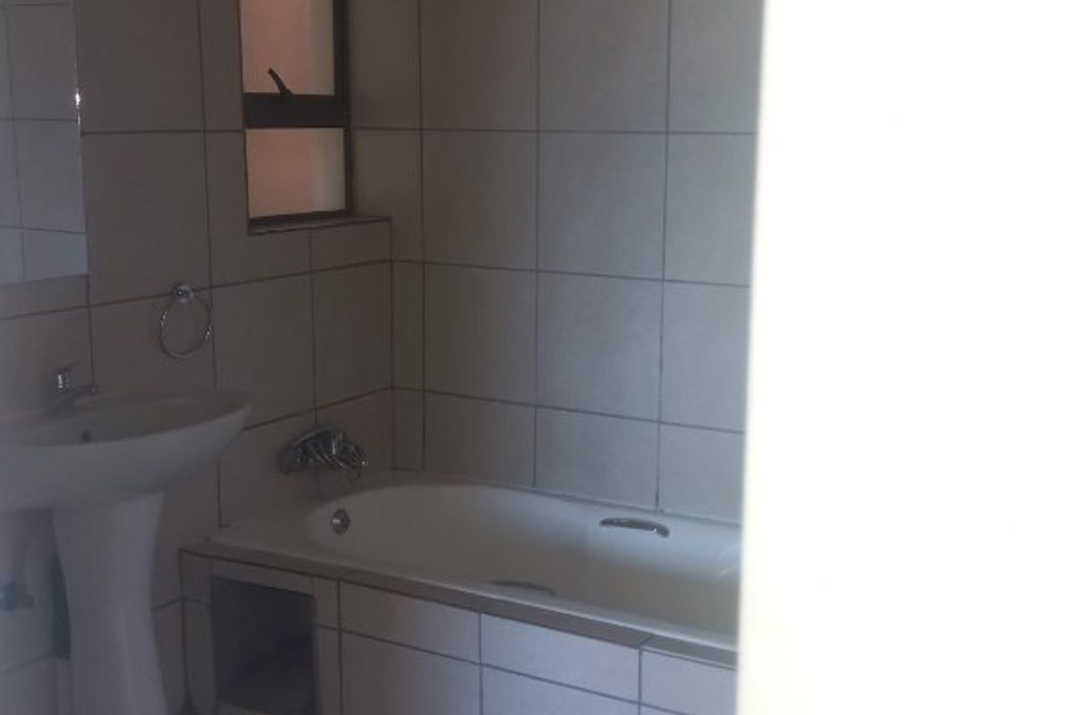 A functional bathroom featuring a pedestal basin, bathtub, and neutral floor-to-ceiling tiling.