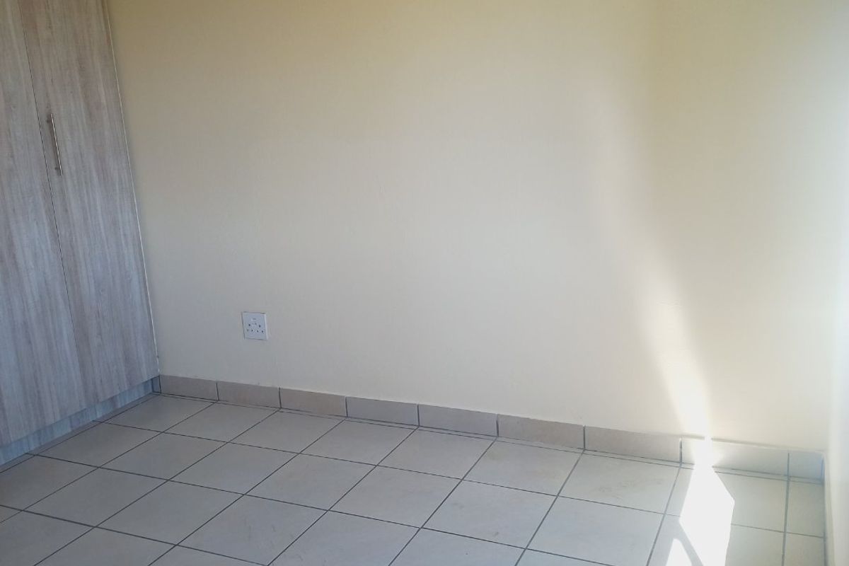 A vacant bedroom featuring neutral walls, light-colored floor tiles, and a built-in wardrobe with wood-grain finish.