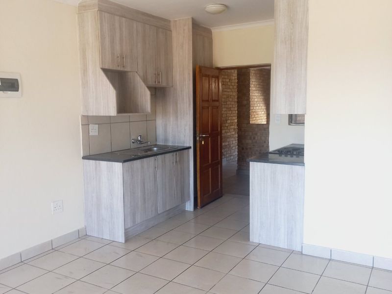 A functional kitchen area featuring light wood-look cabinetry, laminate countertops, a built-in hob, and ceramic floor tiling in an open-plan layout.