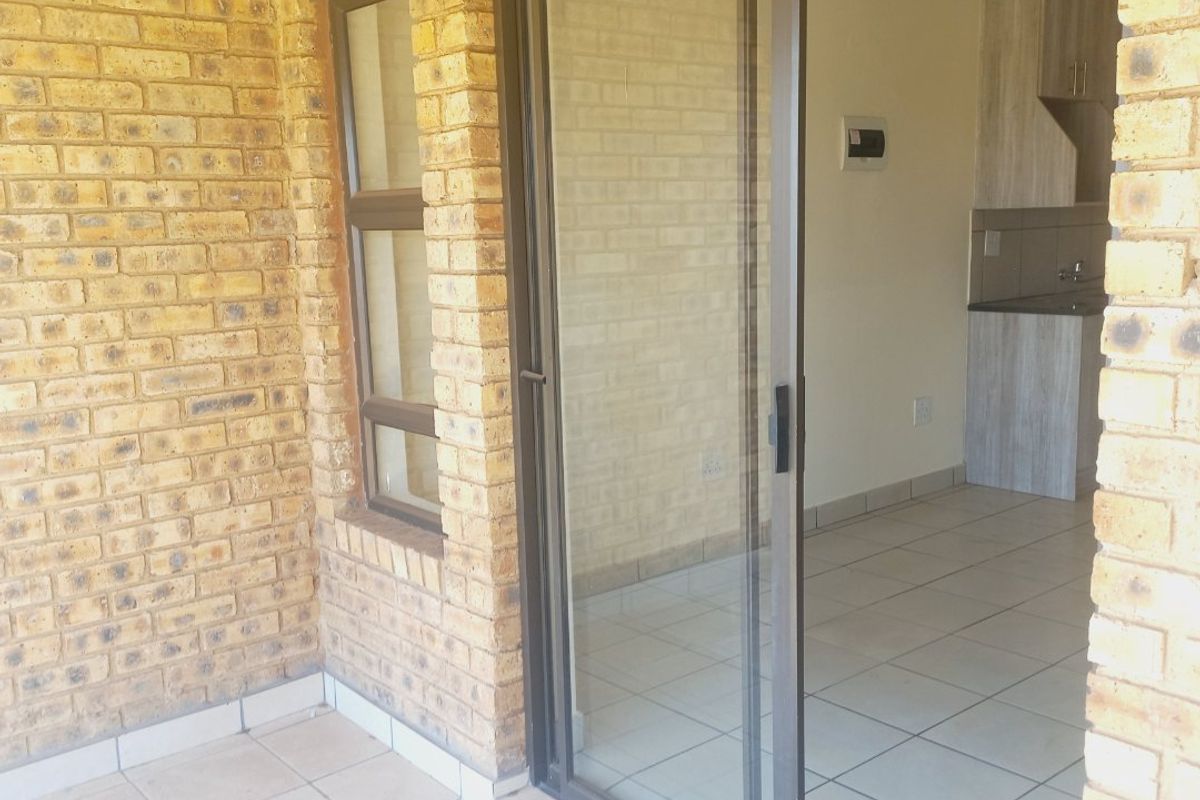 A covered patio area with exposed brickwork and tiled flooring, featuring a sliding glass door providing access to the interior kitchen space.