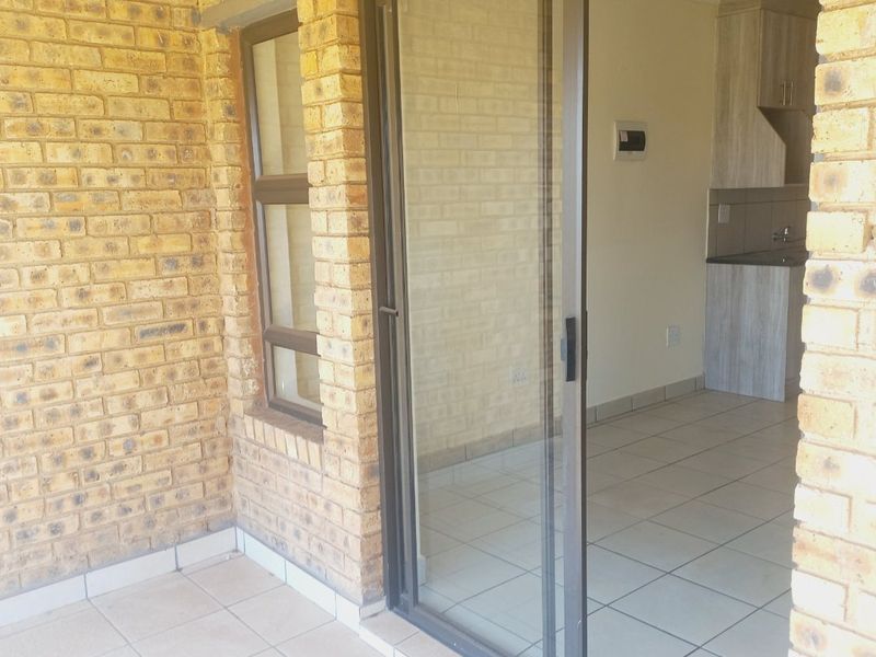 A covered patio area with exposed brickwork and tiled flooring, featuring a sliding glass door providing access to the interior kitchen space.