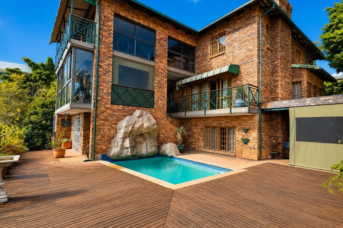Rear exterior view featuring a multi-level brick house with a swimming pool, timber decking, and a balcony.