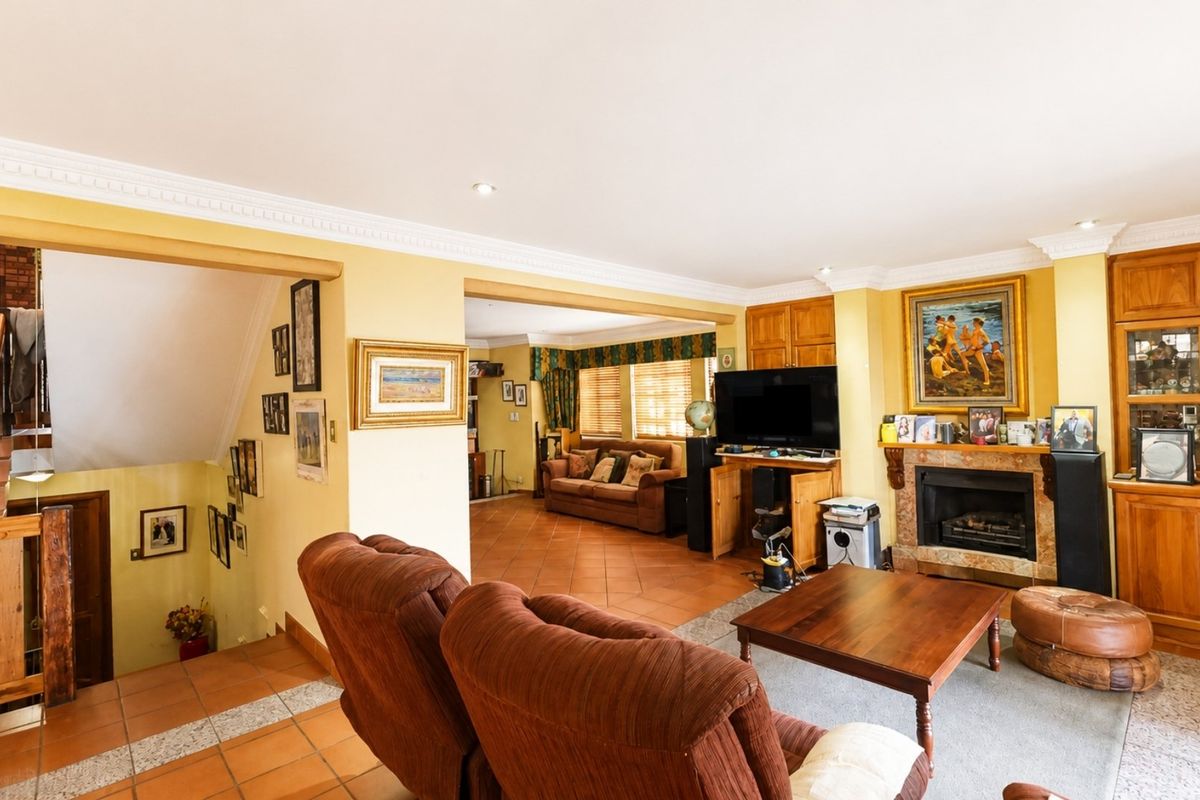 Spacious living area featuring a fireplace, built-in wooden cabinetry, crown molding, and tiled flooring, with an adjacent staircase leading to another level.
