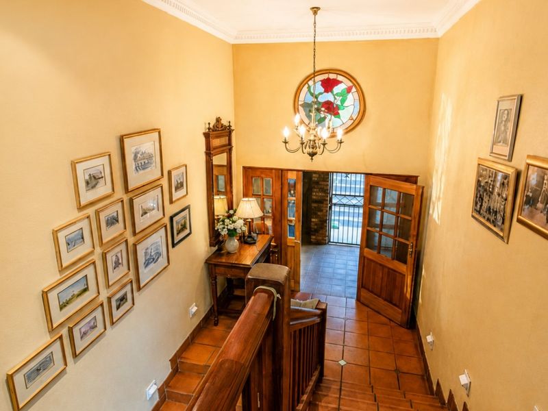 A welcoming entrance hall featuring a wooden staircase, tiled flooring, a decorative stained glass window, and a classic chandelier.
