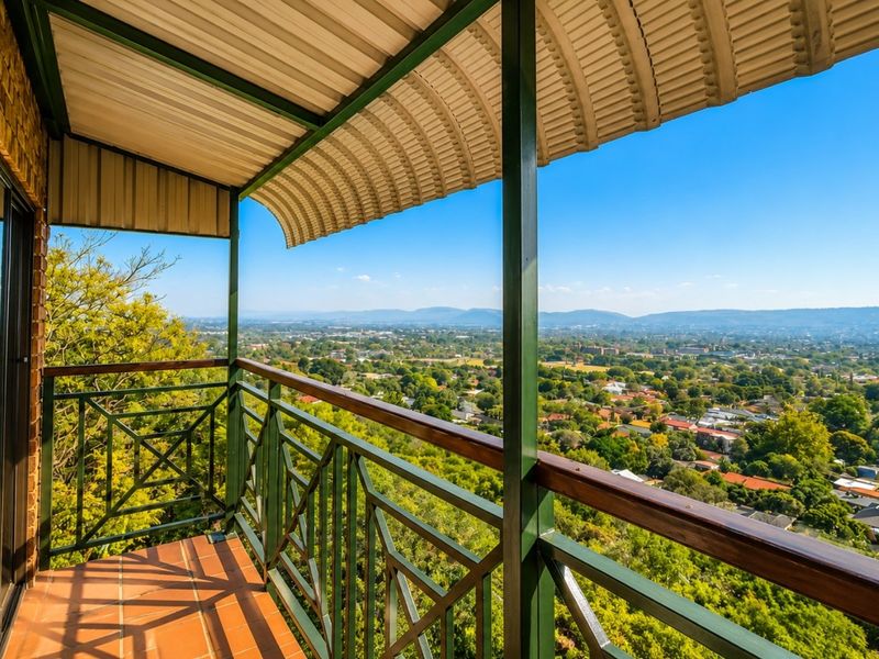 A covered balcony featuring tiled flooring and metal railings, offering expansive elevated views over the surrounding residential area.