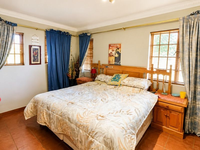 A spacious bedroom featuring tiled flooring, crown molding, and multiple windows with curtain rods, offering a comfortable and functional living space.