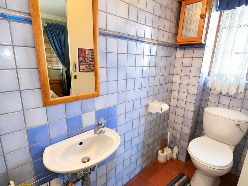 A functional bathroom featuring blue tiled walls, a wall-mounted basin, and a standard toilet, offering a dated aesthetic ready for modernization.