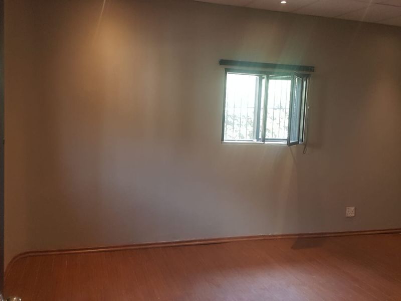 An empty bedroom featuring laminate flooring, recessed ceiling lighting, and a window fitted with security bars.