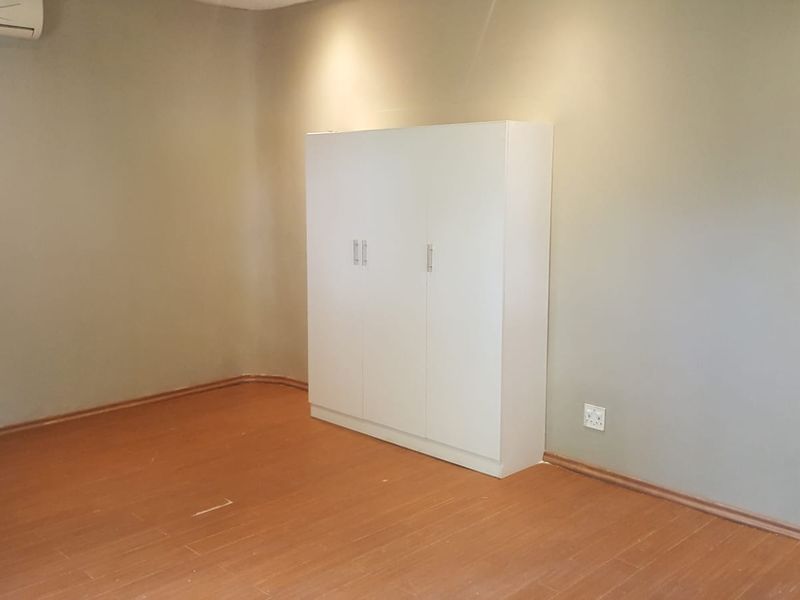 A clean, empty bedroom featuring laminate flooring, a built-in white wardrobe, and a wall-mounted air conditioning unit.