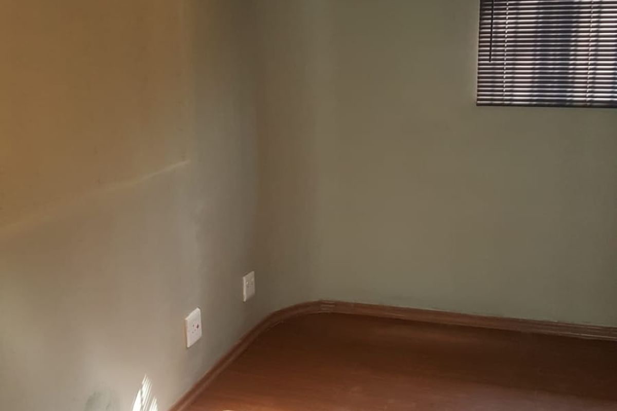 An empty bedroom featuring laminate flooring, a wall-mounted air conditioning unit, and venetian blinds. The room requires minor cosmetic attention to the walls.