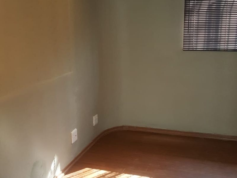 An empty bedroom featuring laminate flooring, a wall-mounted air conditioning unit, and venetian blinds. The room requires minor cosmetic attention to the walls.