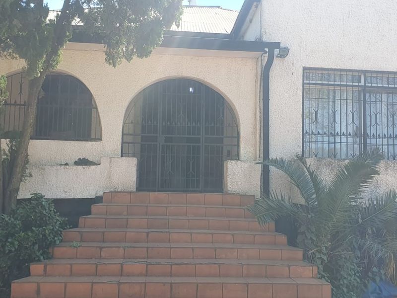 Front elevation of a house featuring a tiled staircase leading to an arched entrance with security gates and arched windows with security bars.