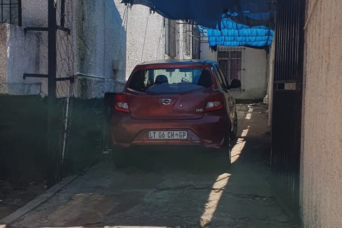 A narrow side or rear driveway area featuring a concrete surface, perimeter wall with security fencing, and a temporary overhead shade structure.
