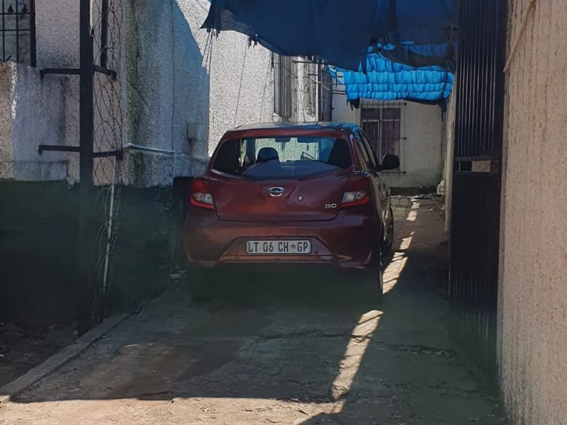 A narrow side or rear driveway area featuring a concrete surface, perimeter wall with security fencing, and a temporary overhead shade structure.