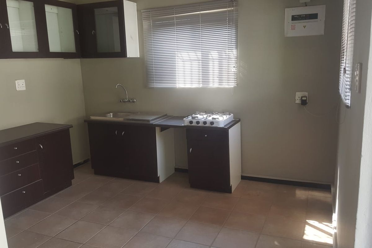 A functional kitchen featuring dark wood cabinetry, a stainless steel sink, a gas hob, and tiled flooring, offering a clean and practical workspace.