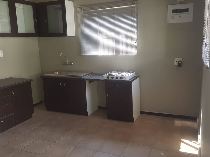 A functional kitchen featuring dark wood cabinetry, a stainless steel sink, a gas hob, and tiled flooring, offering a clean and practical workspace.