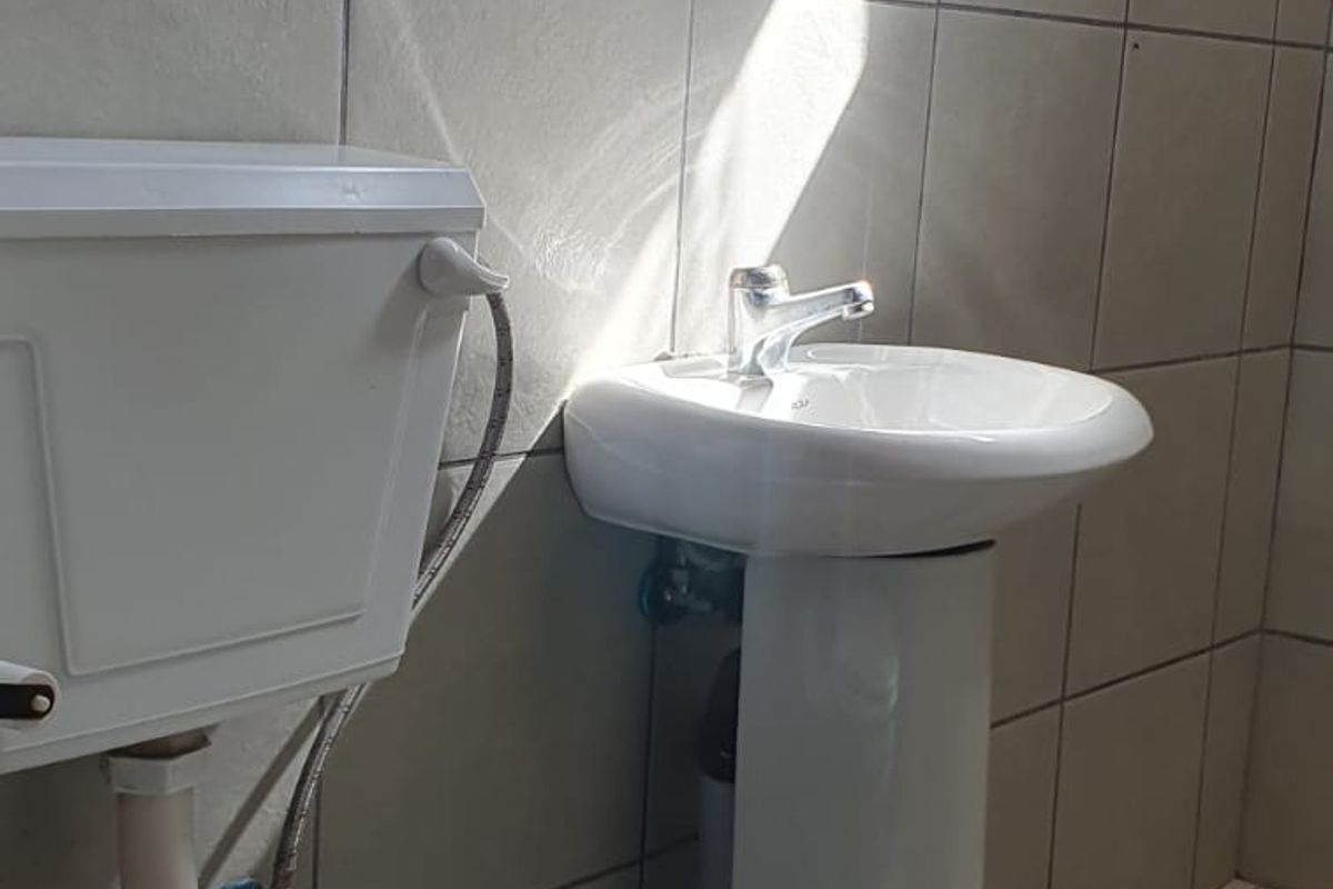 A functional bathroom featuring a pedestal basin, toilet, and tiled finishes, providing a clean and basic utility space.