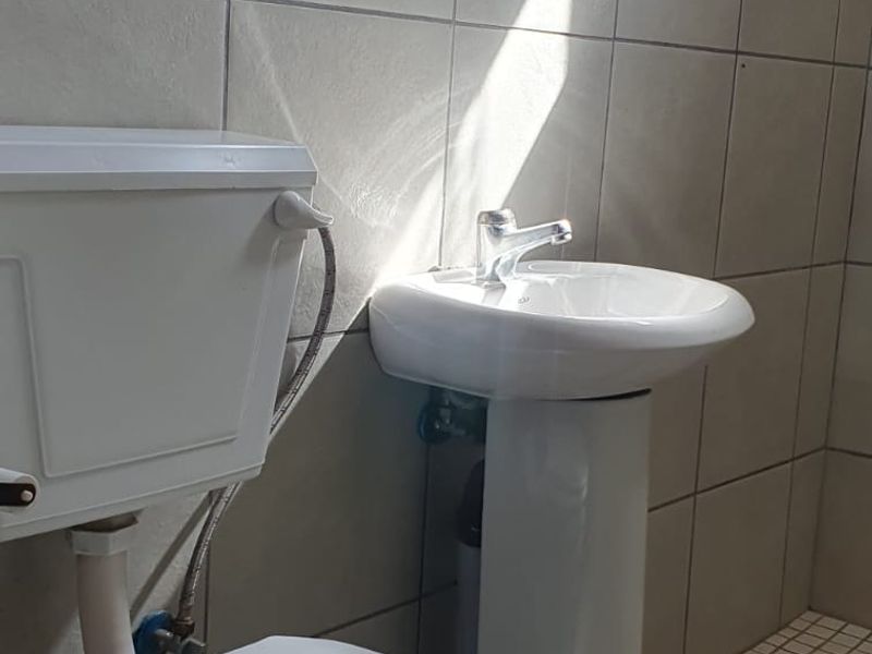 A functional bathroom featuring a pedestal basin, toilet, and tiled finishes, providing a clean and basic utility space.
