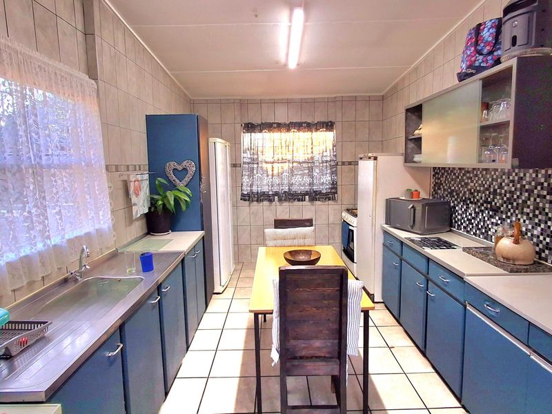 A functional kitchen featuring blue cabinetry, tiled walls and flooring, a stainless steel sink, and built-in cooking appliances.