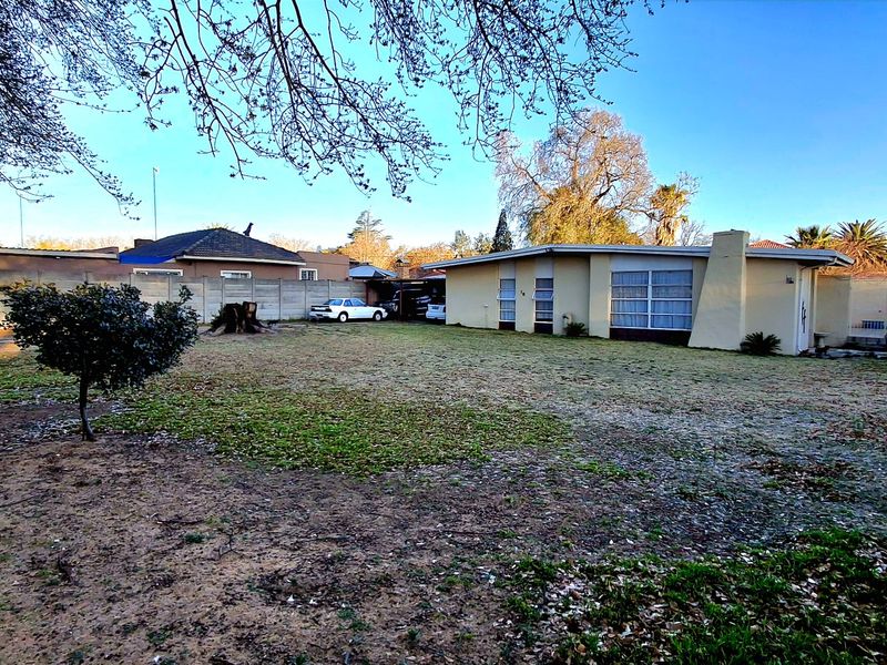Rear view of the property featuring a large garden, precast concrete boundary walls, and a single-story building with an external chimney.