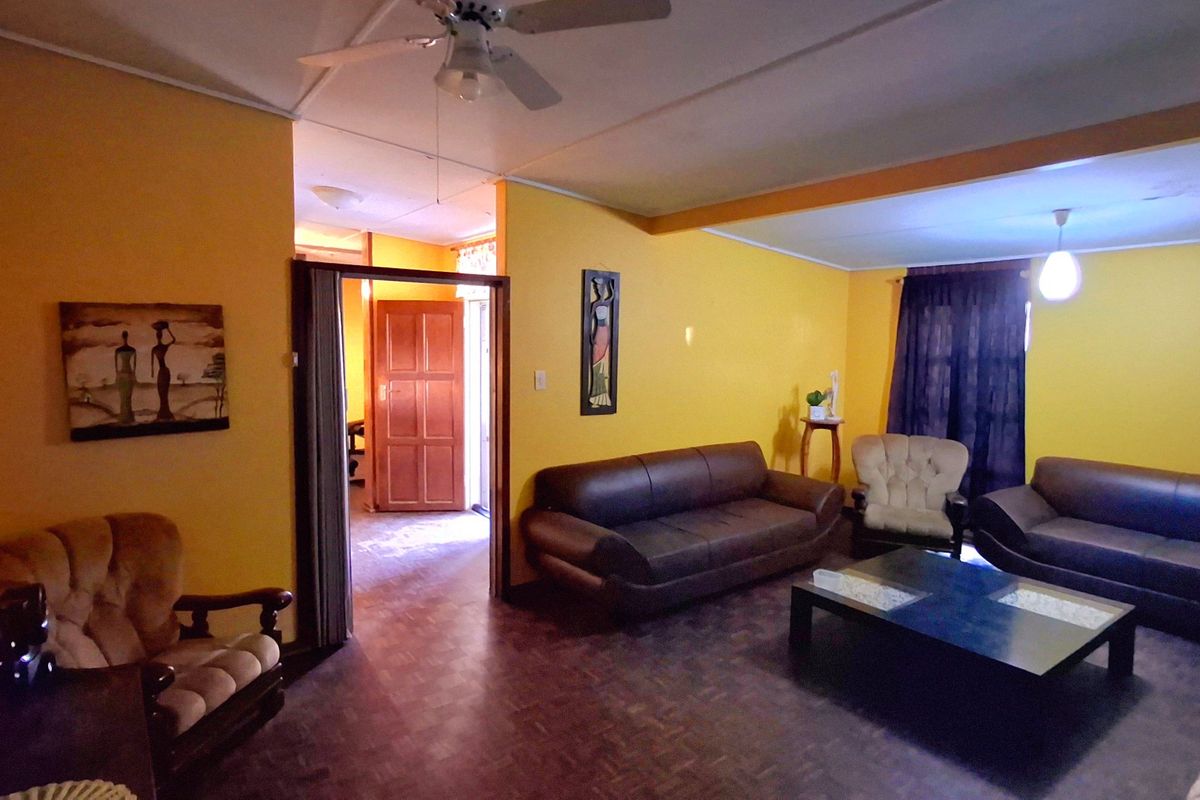 Spacious living room featuring parquet flooring, a ceiling fan, and direct access to an adjacent room through a timber door.