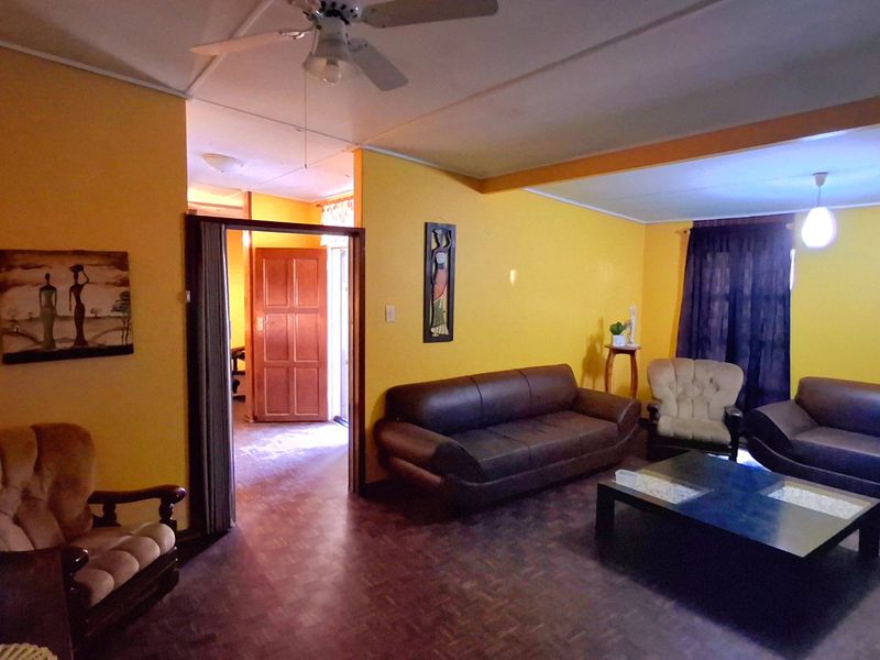 Spacious living room featuring parquet flooring, a ceiling fan, and direct access to an adjacent room through a timber door.