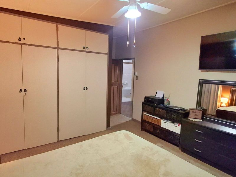A bedroom featuring built-in cupboards, a ceiling fan, and carpeted flooring, with an adjacent view into a bathroom.