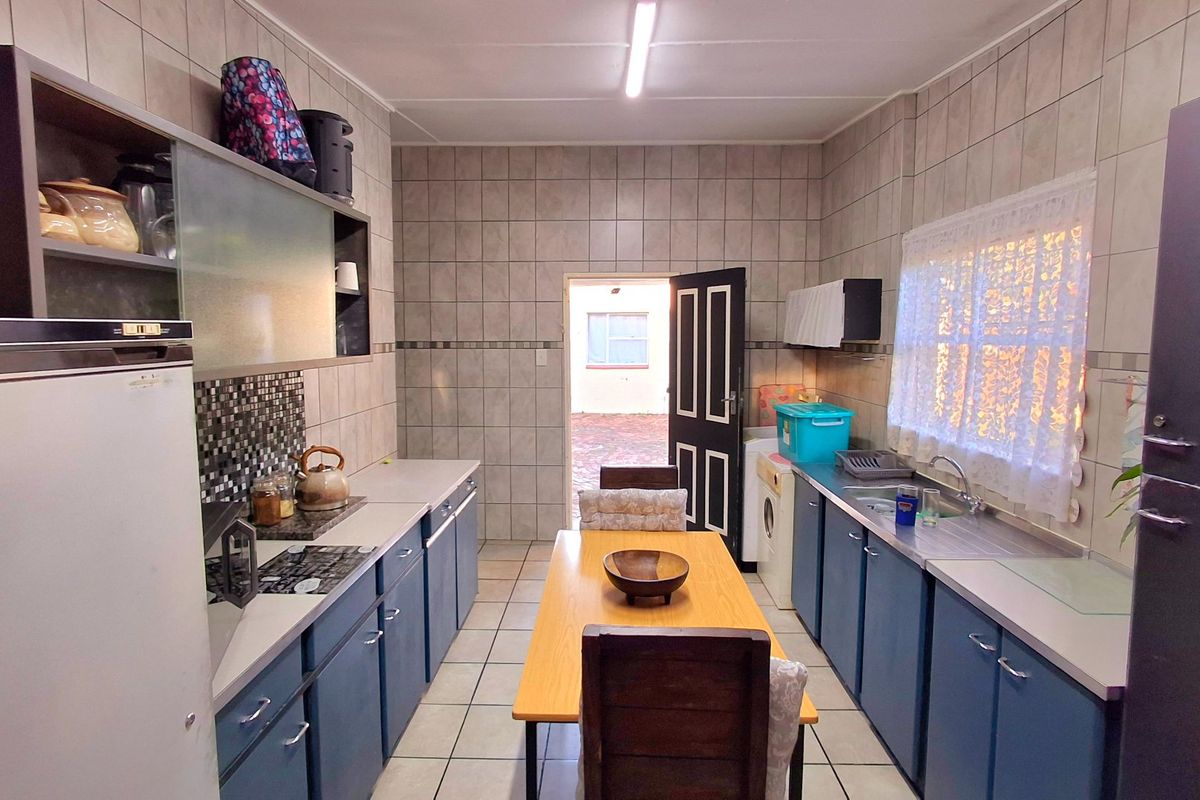 Functional kitchen featuring tiled walls and flooring, ample built-in cabinetry, and a built-in hob, offering a practical layout with direct access to the exterior.