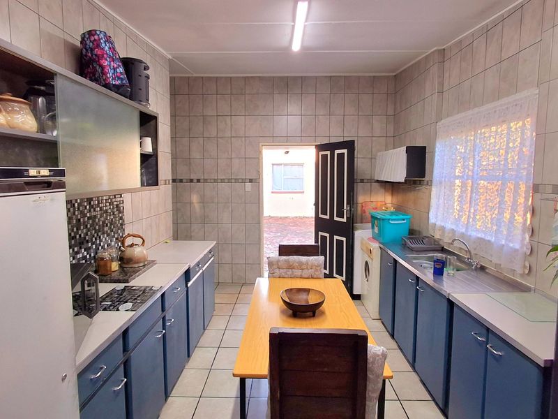 Functional kitchen featuring tiled walls and flooring, ample built-in cabinetry, and a built-in hob, offering a practical layout with direct access to the exterior.