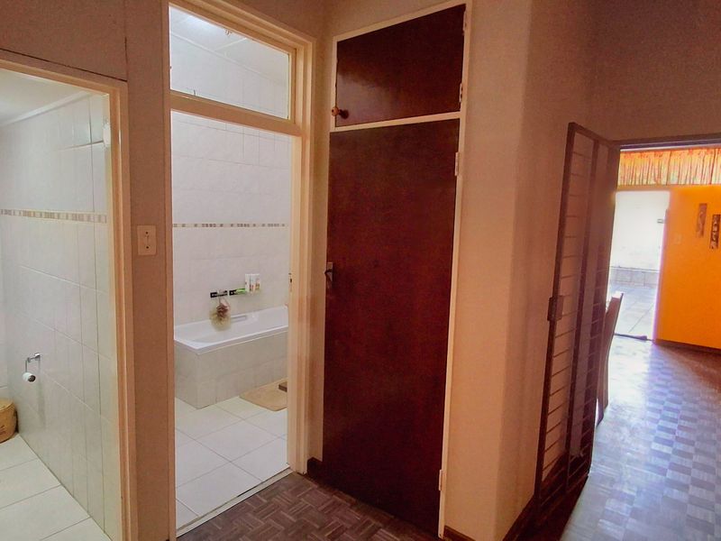A hallway area featuring built-in storage cupboards, providing access to an adjacent bathroom and living space with tiled flooring throughout.